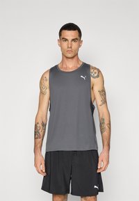 Grå atletisk tanktop med rund hals, prydet med et lille hvidt logo på brystet, sat sammen med løstsiddende sorte shorts.