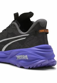 Zapatilla deportiva negra con parte superior de malla texturada, acentos plateados y una suela acolchada morada marcada como "Nitro". Presenta una etiqueta de temporada de PUMA.