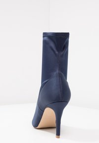Marinblå satinankelboot med en avsmalnande hög klack, slät yta och sömlös design som framhäver en elegant silhuett och subtila sömnadsdetaljer.