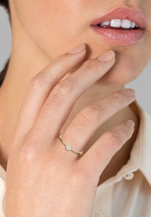 Goldring mit einem floralem Cluster aus kleinen weißen Diamanten, auf einem schlanken Band gesetzt. Hand in der Nähe des Gesichts positioniert, mit natürlichen Hauttönen.