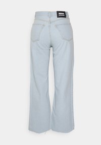 Jeans amplos de cor azul clara feitos de denim. Apresentam uma cintura alta, dois bolsos traseiros e um rótulo da marca preto perto da cintura.