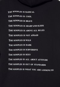 Sudadera negra con capucha que presenta texto blanco con varias frases dispuestas verticalmente. El material parece suave y tiene una textura lisa.