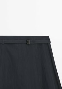 Sort højhalset nederdel med syddelpaneler og et matchende tyndt bælte med en rektangulær metalspænde.