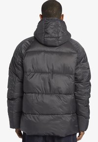 Puffjacka i mörkgrått med ett kviltat mönster, huva och en mjuk, glänsande textur. Bakdelen visar en enkel, strömlinjeformad siluett.