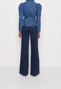 Giacca di jeans con maniche gonfie, vita con cintura e tonalità blu scuro, abbinata a pantaloni in jeans blu scuro a gamba larga.