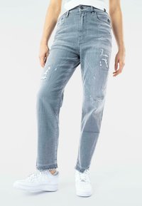 Jeans de mezclilla gris claro con detalles desgastados y un corte holgado, combinados con zapatillas blancas. Presentan una cintura alta y dobladillos deshilachados.