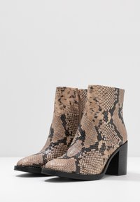 Snakeskinn ankle boots i beige och svart, med spetsig tå och en medelhög blockklack. Har en sidog zip och texturerad yta.