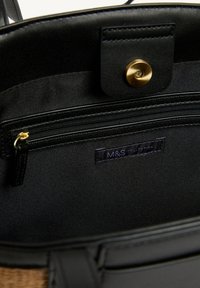 Sac à main en tissu noir avec ferrures dorées. L'intérieur comprend une poche zippée et une étiquette avec la mention "M&S Collection". Texture lisse avec un design structuré.
