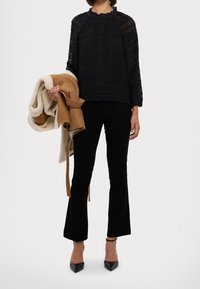 Blusa nera a trama con scollatura arricciata, abbinata a pantaloni neri a zampa d'elefante. Tiene una giacca in pelle beige e foderata in pile crema. Tacchi neri.