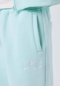 Pantaloni della tuta blu chiaro con tasca laterale e logo star ricamato bianco con "PXP" sulla coscia.