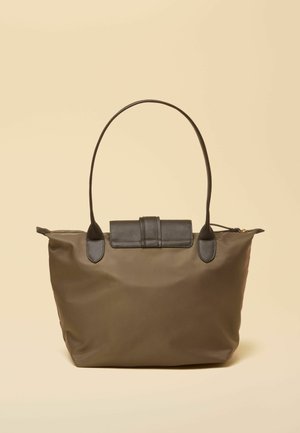 Braune Tragetasche mit langen dunklen Griffen und klappbarem Verschluss, vor einem schlichten beigen Hintergrund.