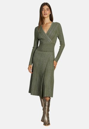 Vestido envolvente verde, con canales, de manga larga, cintura definida, largo hasta la mitad de la pantorrilla y falda acampanada; combinado con botas de vaquero metálicas.