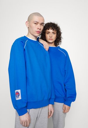 Bright blue sweatshirts with white accents, featuring a logo patch on the sleeve. Ribbed cuffs and relaxed fit complete the design.