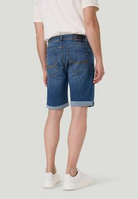 Dunkelblaue Jeansshorts mit umgeschlagenen Saum, ausgestattet mit Gesäßtaschen und kontrastierenden Nähten, getragen mit einem beigen Hemd und weißen Sneakers.
