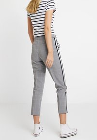 Grå och vit randiga, ankel-långa byxor med svarta sidosträck. Matchas med vita hög-top sneakers och en randig skjorta.