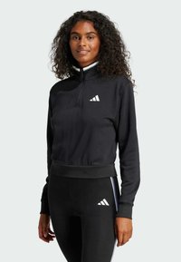 Svart sporttröja med hög krage, dragkedjestängning och vit logotyp. Tillsammans med matchande svarta leggings med sidosträck.