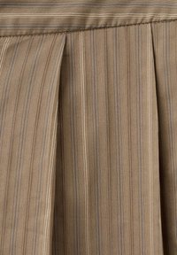 Tissu beige avec de fines rayures verticales bleues et blanches, présentant des plis sous une couture horizontale.