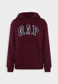 Sudadera burdeos con un gran logotipo bordado de "GAP" en azul marino. Incluye un bolsillo frontal y capucha con cordones. Textura suave, corte relajado.