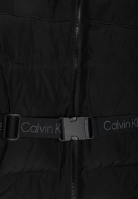 Gilet imbottito nero con zip frontale, caratterizzato da una texture trapuntata, una fascia nera a contrasto con la scritta "Calvin Klein" e una fibbia in plastica.