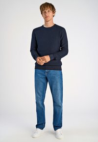 Marineblauer Strickpullover mit strukturiertem Muster, gerippten Bündchen und Taillenbund, kombiniert mit hellblauen, geraden Jeans und weißen Sneakers.