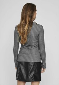 Top gris de manga larga con diseño ajustado, combinado con una minifalda de cuero negra. Ambas prendas tienen texturas suaves y una silueta estilizada.