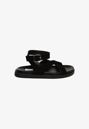 Zwarte sandalen met een gladde synthetische bovenkant, gekruiste banden, een verstelbare gesp en een gestructureerde rubberen zool voor grip.