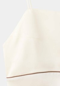 Crop top couleur crème avec fines bretelles et une bordure marron le long du bas sur un fond clair.