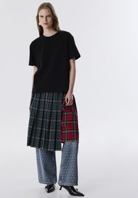 Zwarte katoenen t-shirt gecombineerd met een gelaagde geruite rok in groen en rood, in combinatie met lichtblauwe denim broek met zilveren studs.