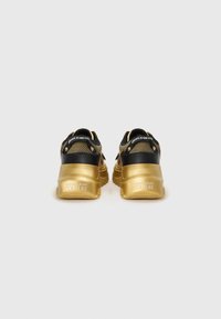 Sorte og guld sneakers med mesh-overdel, kraftige guld såler og præget branding på hælen, der fremviser et dristigt design.
