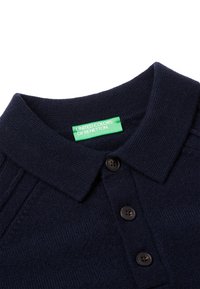 Tmavě námořnická modrá pletená polo košile s límcem a třemi černými knoflíky a zelenou cedulkou s nápisem "United Colors of Benetton."