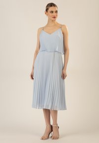 Helles blaues, plissiertes Kleid mit dünnen Trägern, V-Ausschnitt, geschichteter Gestaltung und fließendem Stoff. Kombiniert mit silbernen Riemchen-Highheels.