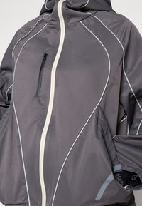 Gray hooded jacket with contrasting white zipper and stitching. Features a zippered pocket and a loose, textured design for comfort.
