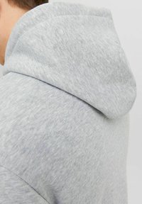 Gray hoodie made of soft, textured fabric, featuring a rounded hood and seamless shoulder design. The fabric shows a subtle heather pattern.