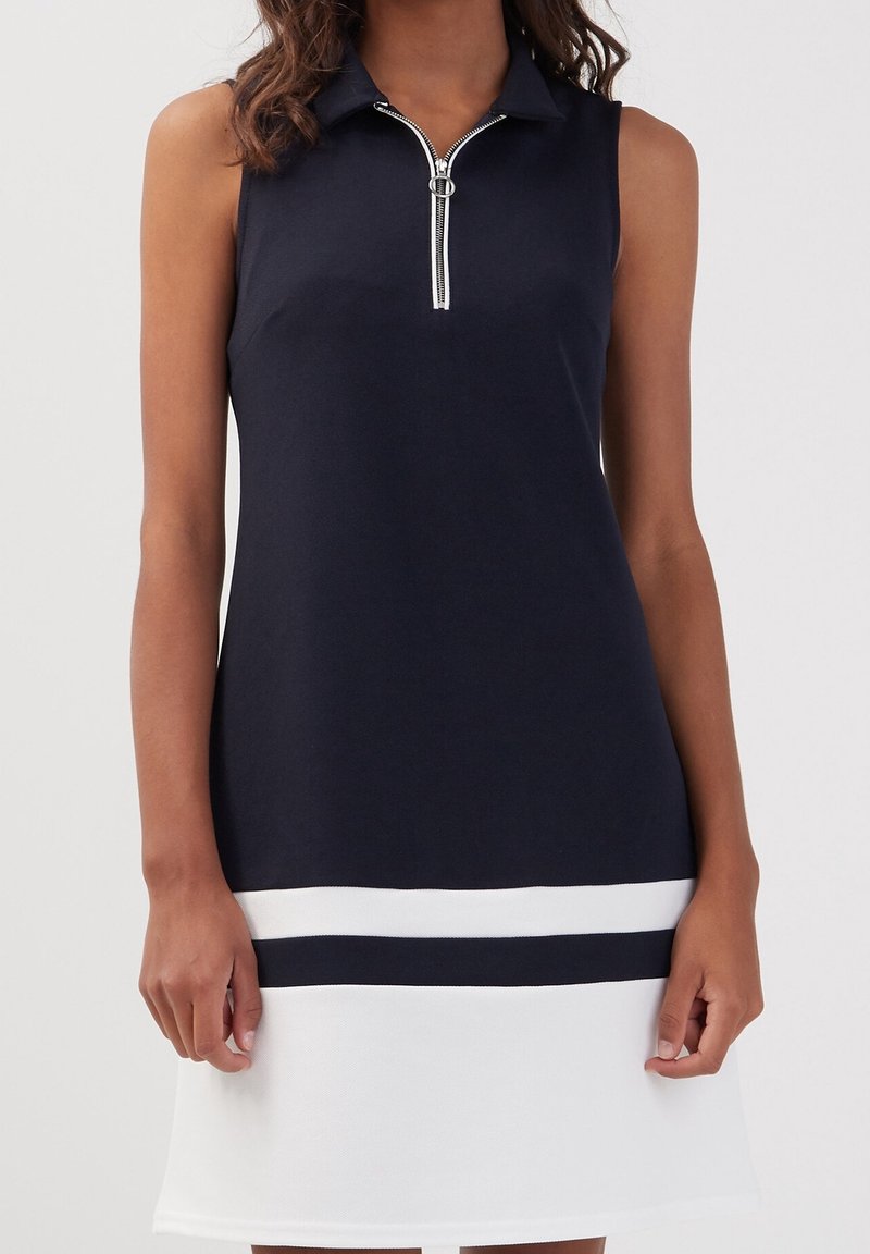 Robe polo sans manches en bleu marine, avec un col zippé, un ourlet blanc orné de rayures bleues marines, confectionn ée dans un tissu lisse et texturé.