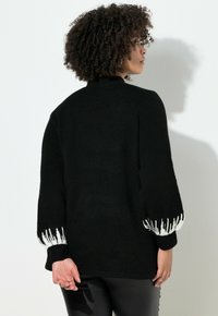 Suéter negro con cuello alto y mangas voluminosas. Diseño de acento blanco en los puños que crea contraste. Textura suave y ajuste relajado.