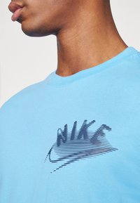 T-shirt in cotone blu con un grande logo Nike stilizzato in nero con spessore delle linee variabile, scollatura a girocollo e maniche corte.
