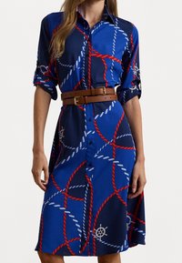Modré košilové šaty vyrobené z látky s námořnickým řetězcem v červené a bílé barvě, s hnědým páskem a akcentem v podobě lodního kormidla. Krátké rukávy.