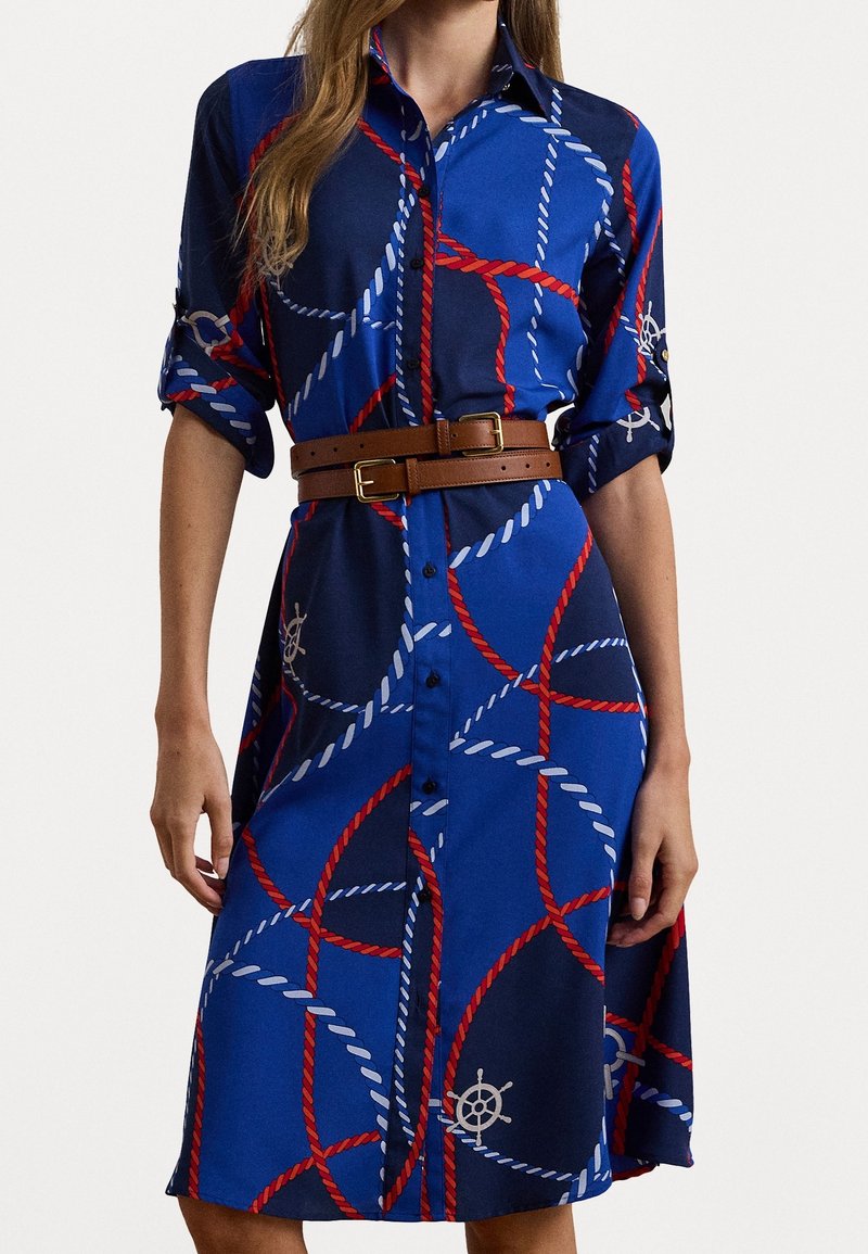 Modré košilové šaty vyrobené z látky s námořnickým řetězcem v červené a b�ílé barvě, s hnědým páskem a akcentem v podobě lodního kormidla. Krátké rukávy.