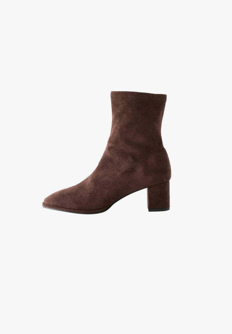 Botin en suède marron avec un bout pointu et un talon épais. La tige est lisse avec un design sans coutures et des détails de couture subtils.