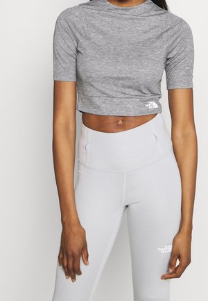 Kobieta w dopasowanym, szarym krótkim T-shircie i jasnoszarych legginsach z wysokim stanem z logo The North Face na obu elementach odzieży.