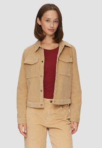 Kastanjebruine corduroy jacket met twee borstzakken, drukknoopjes en een cropped ontwerp. Gekocht over een burgundy shirt en gecombineerd met bijpassende broek.