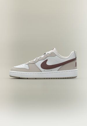 White and beige low-top Nike sneaker with brown swoosh logo and white laces on neutral background, side view showing sole texture.