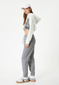 Witte hoodie met een grafisch ontwerp, grijze sweatpants met een trekkoord en jogger manchetten, gecombineerd met witte sneakers met zwarte accenten.