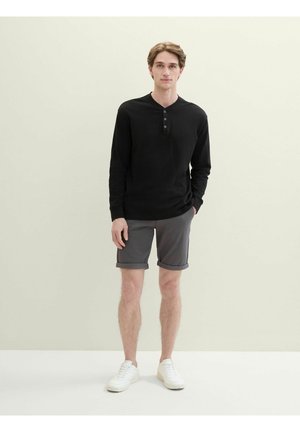 Schwarzes Langarm-Henley-Shirt mit drei Knöpfen, graue Shorts und weiße Sneakers. Das Shirt hat einen strukturierten Stoff und eine entspannte Passform.