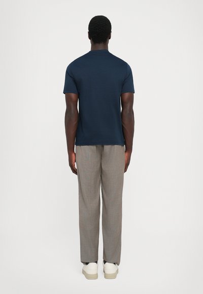 Tricou din bumbac de culoare bleumarin, cu mânecă scurtă, asortat cu pantaloni deschiși la culoare, cu model, și adidași albi, văzut din spate.