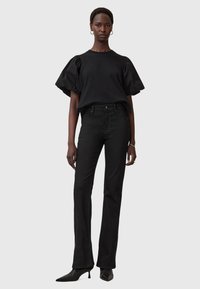 Top nera con maniche a sbuffo abbinato a jeans neri svasati. Tessuto liscio, design aderente e tacchi neri a punta completano l'outfit.