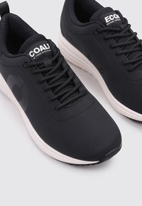 Zapatillas deportivas negras con una parte superior sintética suave, cordones negros texturizados, suela blanca en contraste y un logo en el costado. Diseño de punta cerrada.