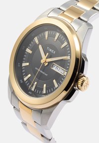 Zegarek Timex z czarną tarczą, złotą stalową obręczą, bransoletą w kolorze srebrno-złotym, wodoodporny, z wyświetlaczem daty na godzinie 3.