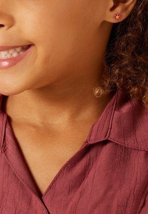 Pink flower-shaped stud earring on a child's ear, paired with a textured mauve shirt. Close-up of the face and upper chest.
