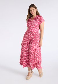 Maxi dress in pink with a zigzag pattern, short sleeves, and a wrap design, paired with woven wedge sandals. Smooth, lightweight fabric.